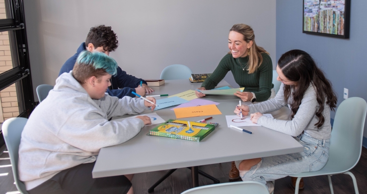 3 students and 1 teacher sitting at a table. The students are drawing.