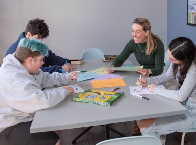 3 students and 1 teacher sitting at a table. The students are drawing.